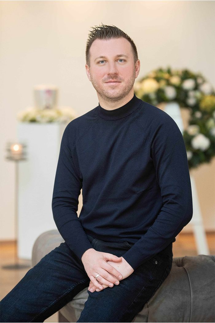 Torsten Schröder sitzt auch einer Couchlehne, im Hintergrund sind Blumenkranz, Kerze und Urne