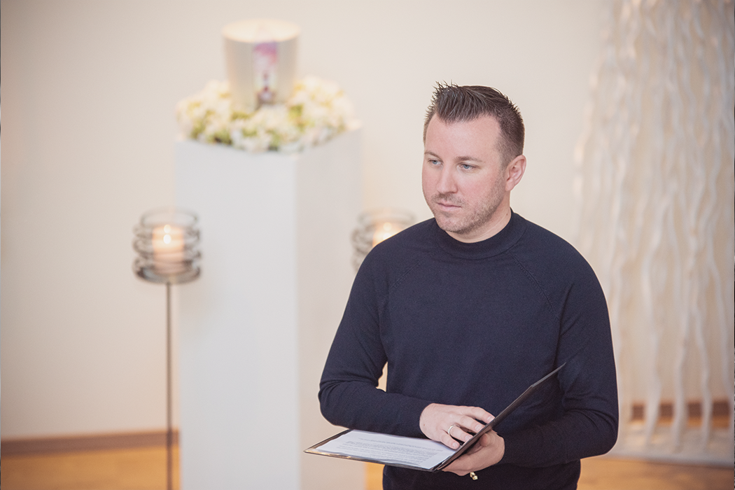 Trauerredner Torsten Schröder hält eine Trauerrede, im Hintergrund ist eine Urne mit Blumenkranz & zwei Kerzen